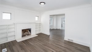 An empty living room with built-in shelves, a white fireplace, and laminate flooring.