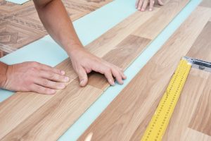 Laminate flooring installers are installing laminate hardwood planks over a soundproofing underlayment, and insulation.